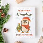 Christmas card with a penguin holding a tree, surrounded by festive decorations on a white background.