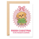 Christmas card with a dog holding a Christmas tree and a pink bow on a white background.