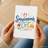 A white greeting card with colorful hand-drawn illustrated design featuring a flower and envelope for irish thinking smaoineamh ort
