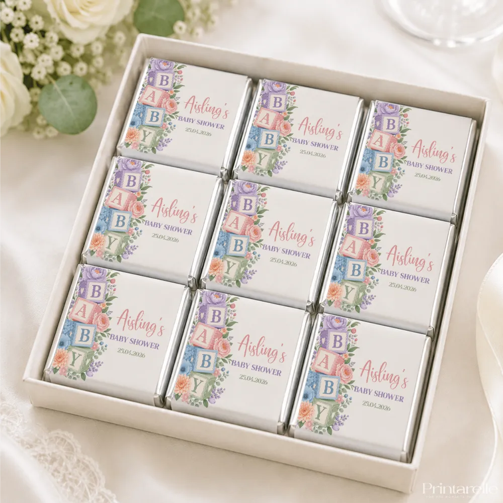 A white gift box of mini neapolitan chocolates with pastel floral wraps and colorful alphabet blocks spelling baby