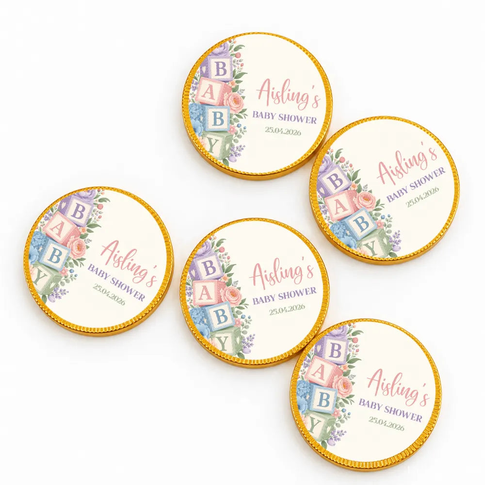 Round gold-edged chocolate coins with pastel floral baby blocks design on cream centers for baby shower gifts