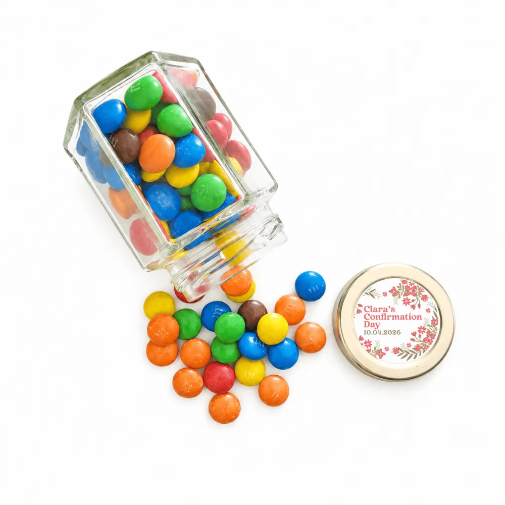 Clear glass hexagonal jar with pale gold twist lid personalised sticker printed filled with colorful m and ms spilling out