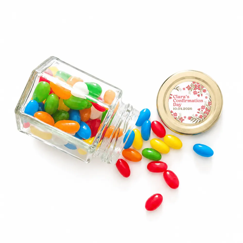 A clear glass hex jar tipped over with colorful jelly beans and a 48mm pale gold twist lid with a personalised sticker printed