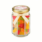 A personalised hex jar favour filled with colorful gummy bears with a 48mm pale gold twist lid and cream ribbon bow