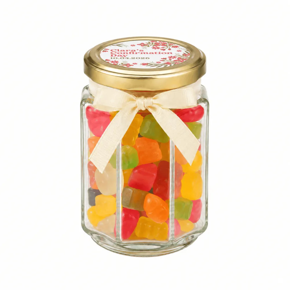 A personalised hex jar favour filled with colorful gummy bears with a 48mm pale gold twist lid and cream ribbon bow