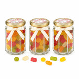 Three personalised hex jars with 48mm pale gold lids and cream ribbons filled with colorful gummies for blossoms grace confirmation