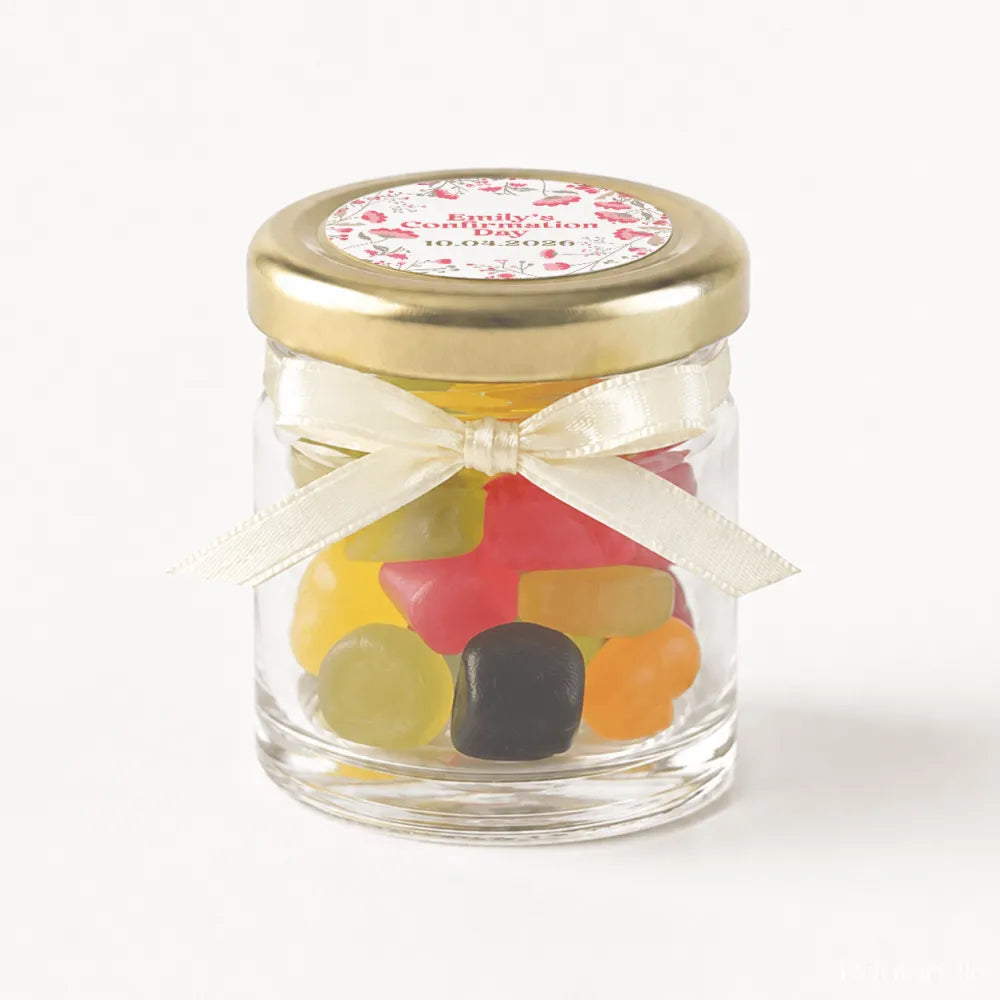 A clear glass mini jar favour with 43mm pale gold twist lid cream ribbon bow and personalised sticker printed label filled with gummies