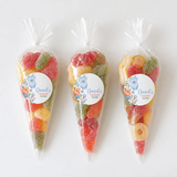 Three clear plastic sweet cones filled with colorful gummy candies and blue onesie labels for christening gifts
