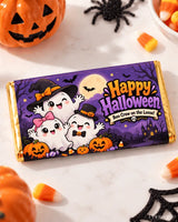 A purple and gold halloween chocolate box wrap featuring cartoon ghosts in witch hats on a spooky night sky 100g bar