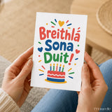 A colorful irish birthday card with sona duit and breithlá sona duit text above a cartoon cake illustration