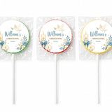 Three personalized round christening lollipop favours with blue floral design gold text and candle shell decorations wrapped in cellophane