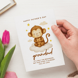 Hand holding a Father's Day card with a monkey illustration and text, next to a pink tulip.