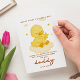 Hand holding a Father's Day card with a yellow duck illustration and text, next to a pink tulip.