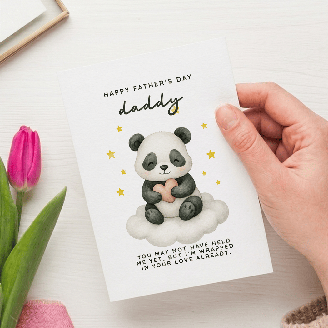 Hand holding a Father's Day card with a panda illustration and pink tulip on a white surface.