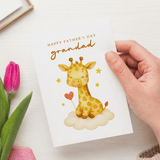 Hand holding a Father's Day card with a giraffe illustration and pink tulips on a white surface.