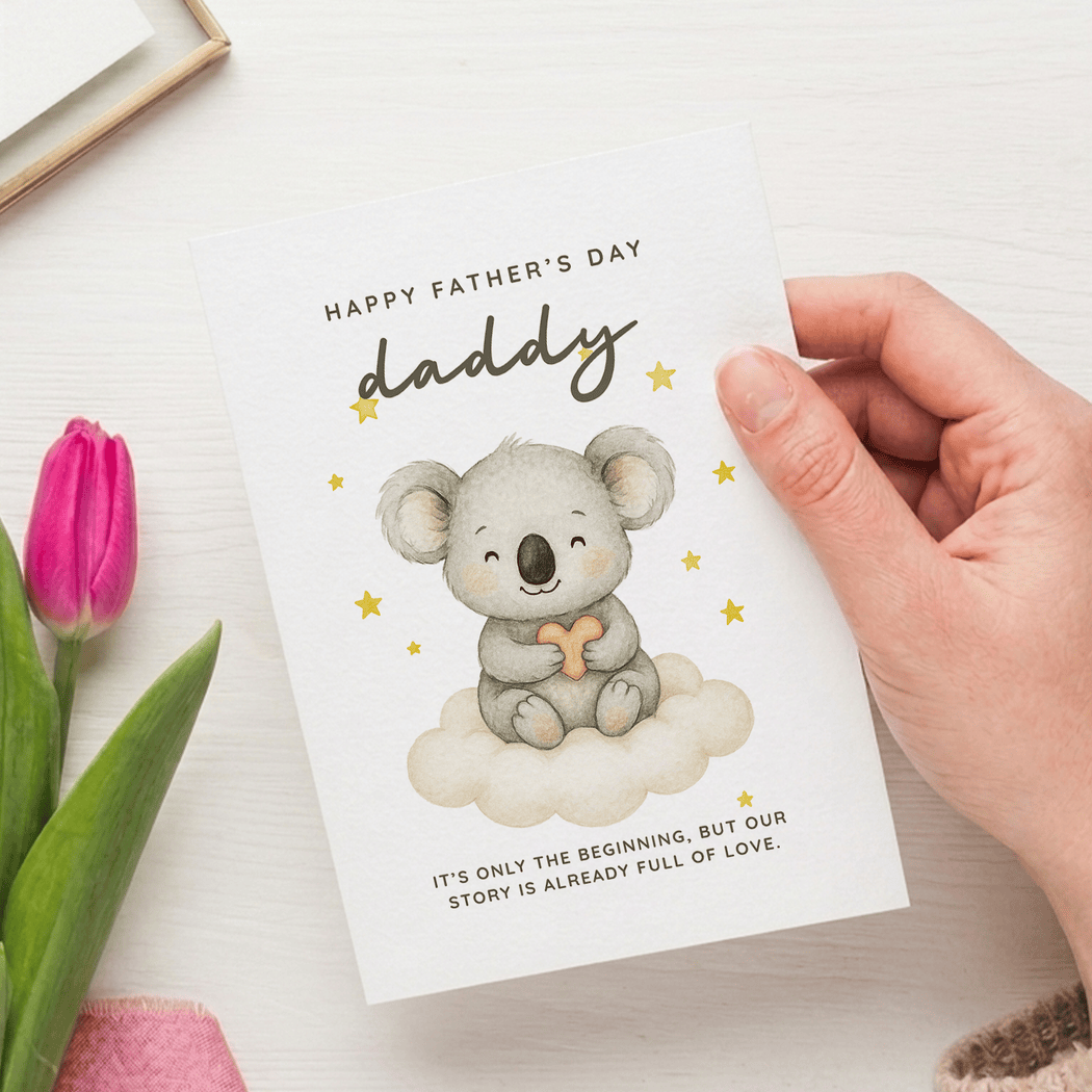 Hand holding a Father's Day card with a koala illustration and pink tulip on a white surface.