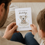 Person holding a Father's Day card with a koala illustration and text.