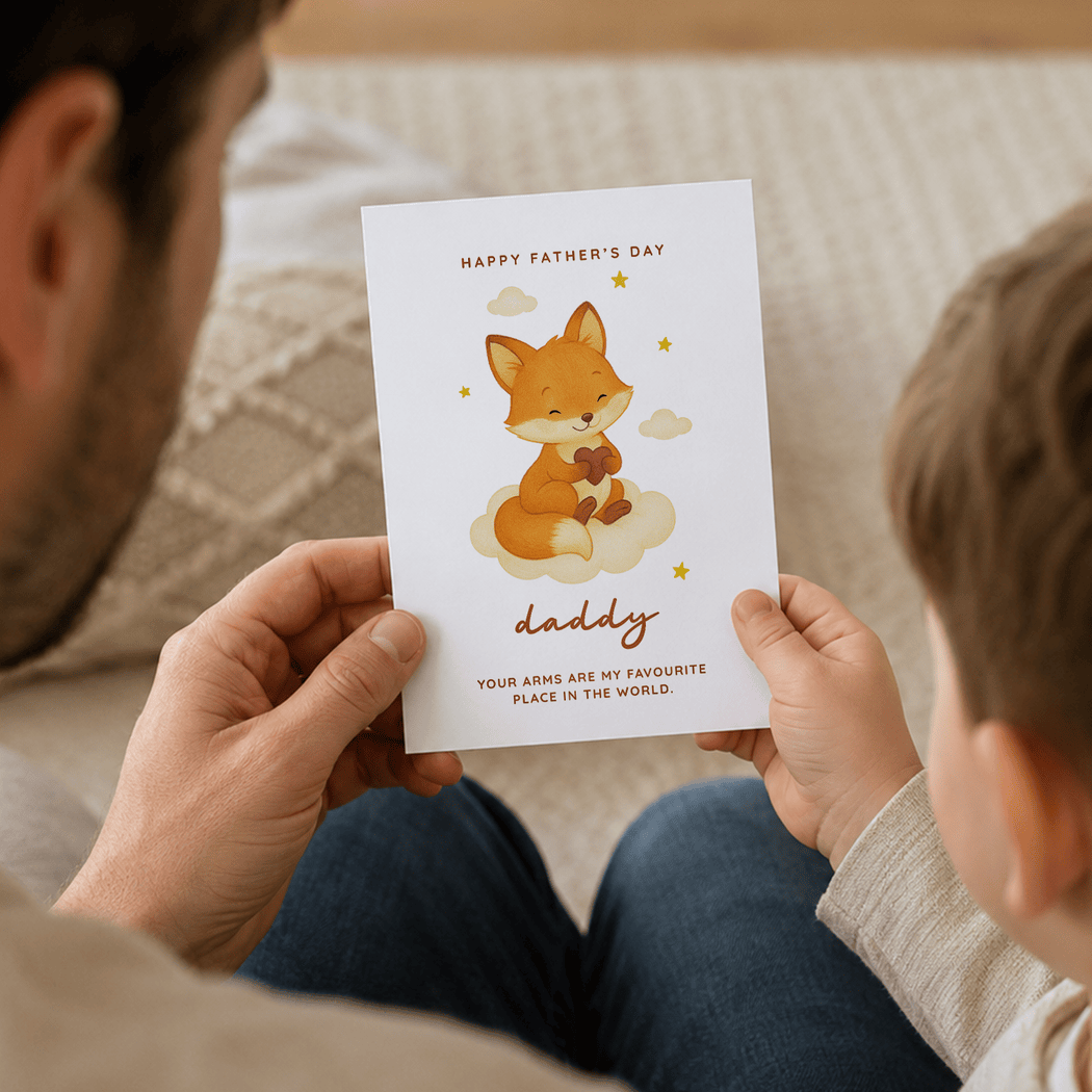 Child holding a Father's Day card with a fox illustration, sitting on a couch with an adult.