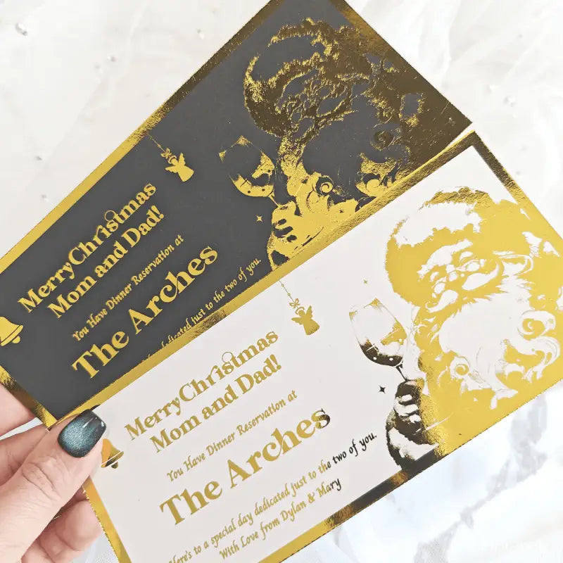 Two Christmas gift cards with gold text and images of a couple, held by a hand.