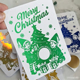 Christmas card with elves and tree design, held by a hand.