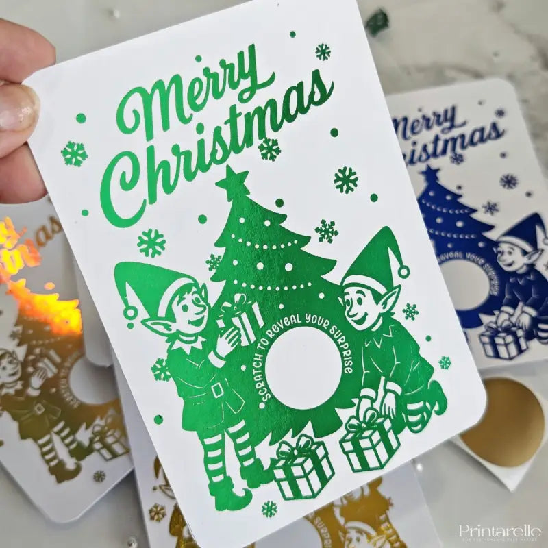 Christmas card with elves and tree design, held by a hand.