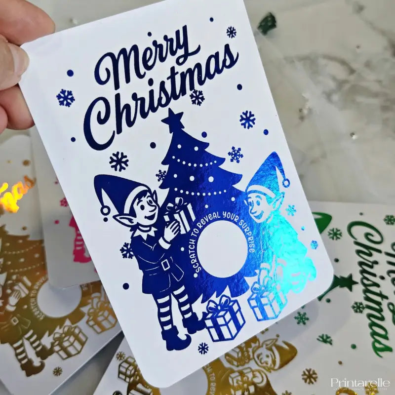 Christmas card with blue elves and tree design, held by a hand.