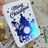 Christmas card with blue elves and tree design, held by a hand.