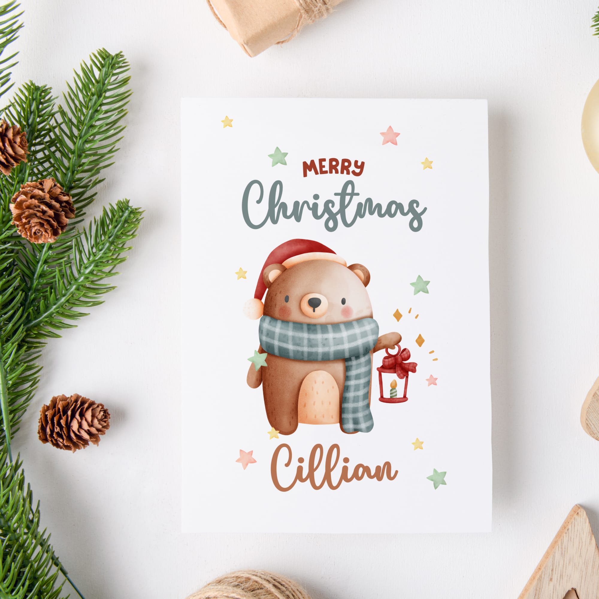 Christmas card with a bear holding a lantern, surrounded by pine branches and pinecones on a white background.