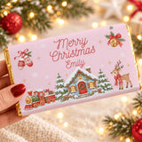 A personalized pink chocolate bar wrap with gold foil showing a festive cottage and steam train scene with merry christmas emily