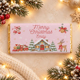 A pink chocolate bar wrap with gold foil featuring a festive christmas scene with a steam train and merry christmas emily message
