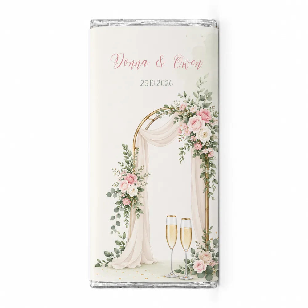 A personalised 40g chocolate bar with a floral arch and champagne flutes wrapped in clear foil for weddings