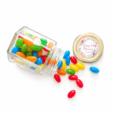 A clear glass jar with a floral wreath gold lid spills colorful jelly beans perfect for wedding favours