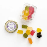 Clear glass jar with gold lid and purple floral wreath sticker filled with colorful gummy candy wedding favours