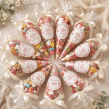 Clear plastic sweet cones filled with colorful gummies tied with white ribbons and coral floral wreath labels for confirmation day