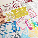 A hand holds a yellow and white north pole express ticket with a gold bow 100g chocolate bar featuring snowy mountains