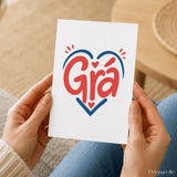 A white irish love card featuring the word grá in bold red script outlined with a blue heart and small hearts