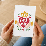 A white grá mór irish love card with a red heart held by golden hands under a yellow crown and green leaves