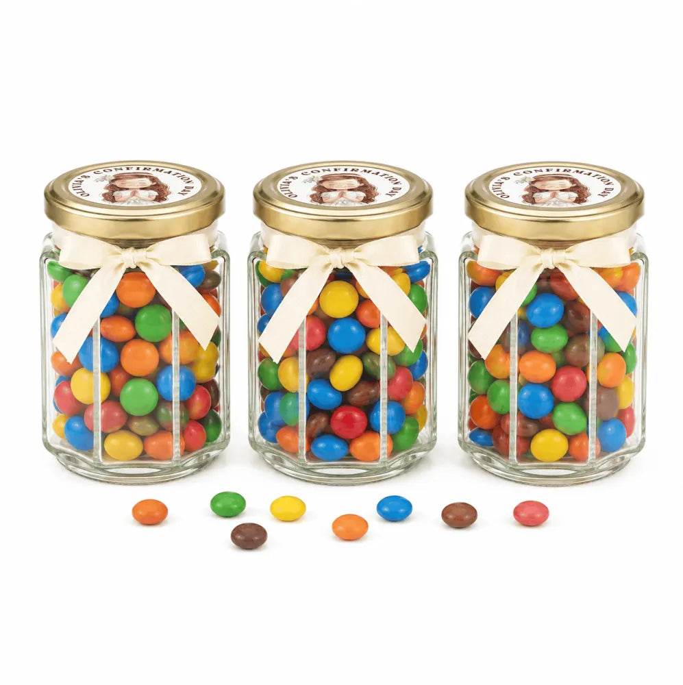 Three personalised hex jar favours with 48mm pale gold lids and cream ribbons filled with colourful m&m’s candies