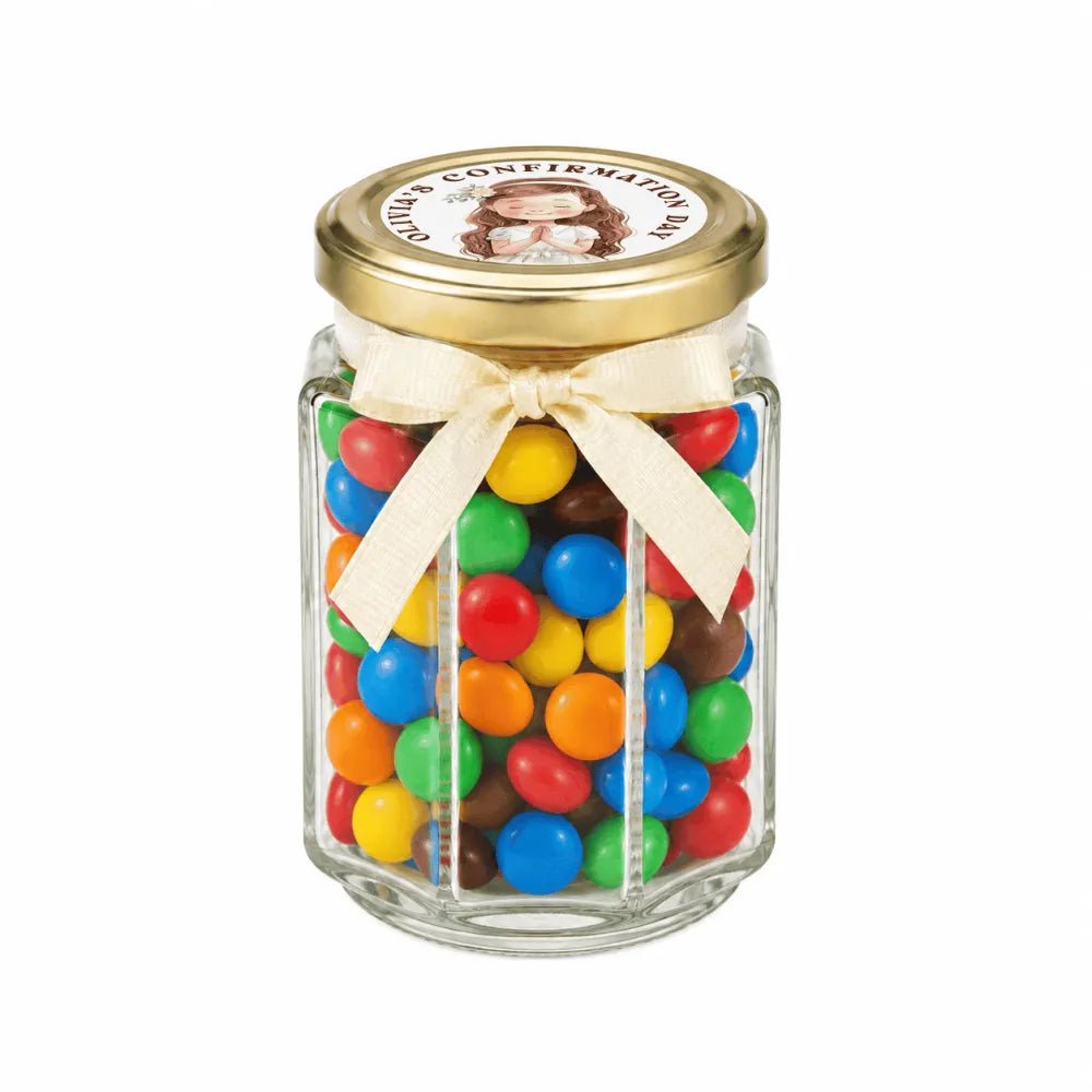 A clear hexagonal glass jar with a 48mm pale gold lid and personalised sticker printed, filled with colorful mms for halo grace confirmation