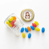 A clear glass mini jar favour with 43mm pale gold twist lid and personalised sticker printed for olivias confirmation day spilling colorful jelly beans
