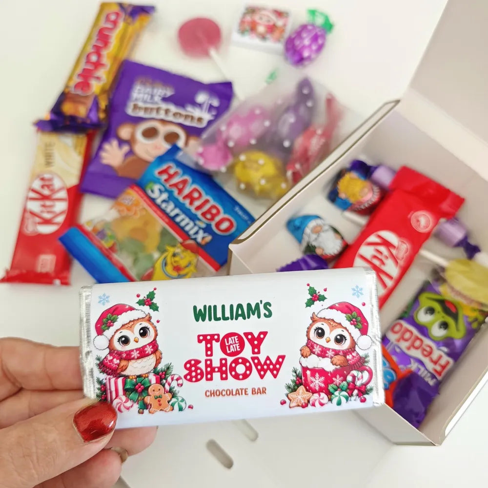 A festive white chocolate bar wrapper with two owls in santa hats and late late toy red lettering for christmas treats