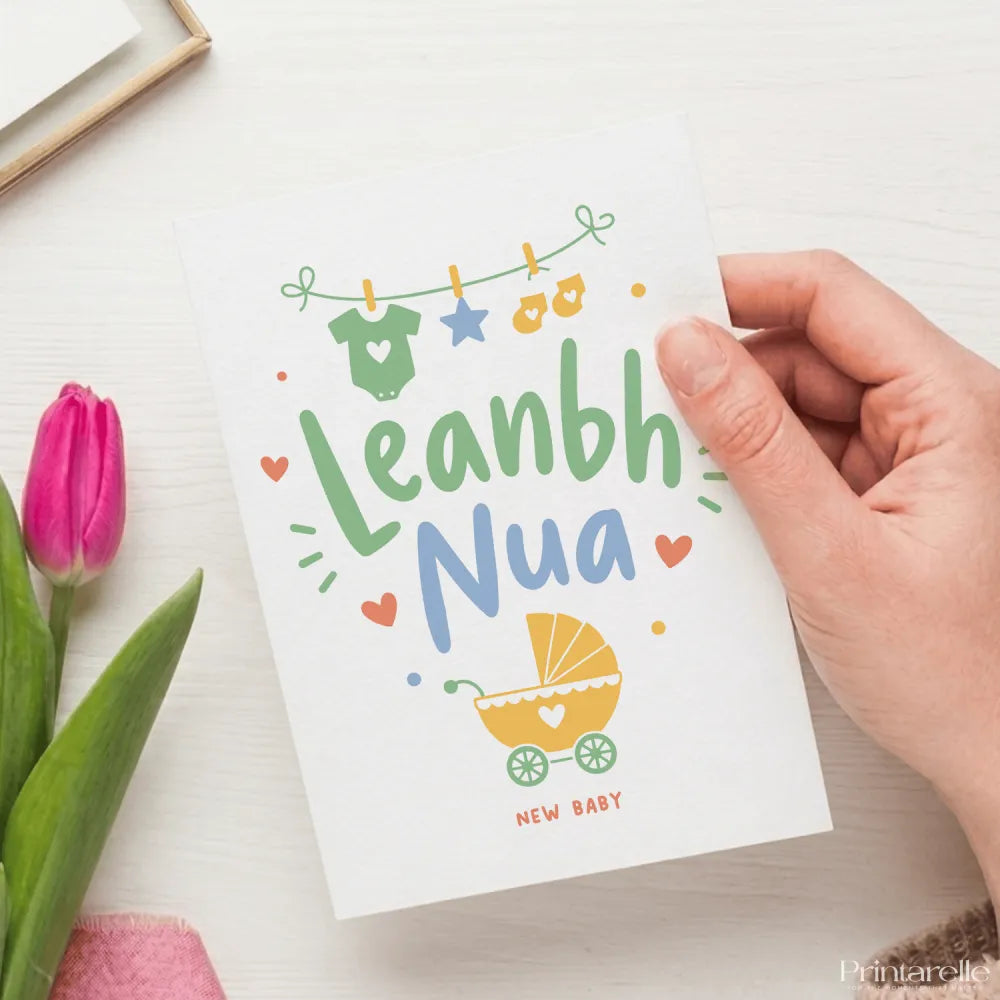 A white leanbh nua baby card with soft green and blue illustrations of a onesie star booties and pram for new baby celebration