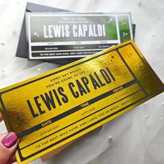 Gold ticket-style card with 'LEWIS CAPALDI' printed on it, held by a hand.