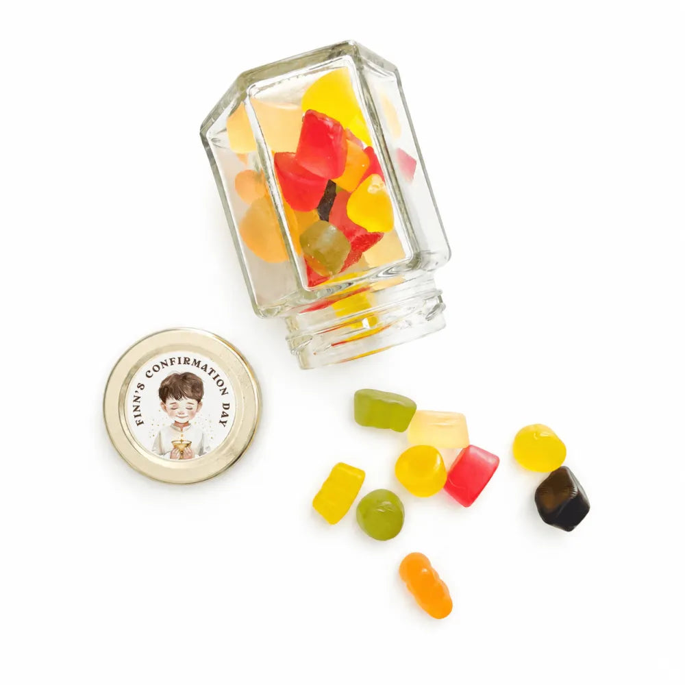 A clear hex jar favour with a 48mm pale gold twist lid spilling colorful gummies with a personalised sticker printed