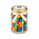 A clear hexagonal glass jar with a 48mm pale gold lid and cream bow filled with colorful mms and personalised sticker printed