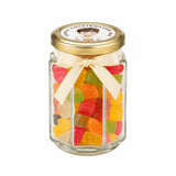 A clear glass personalised hex jar favour filled with colorful gummy bears tied with cream bow and 48mm pale gold lid