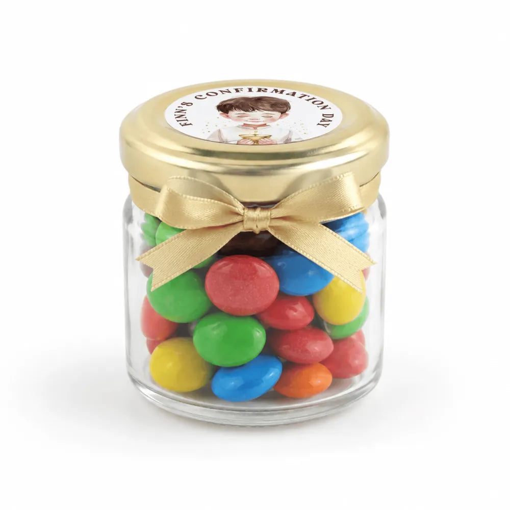 A clear glass mini jar favour filled with colorful candy, featuring a pale gold twist lid and personalised sticker printed label