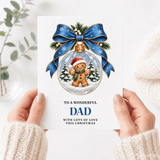 A dad christmas card featuring a gingerbread dad in a glass bauble with santa hat, scarf, blue bow, and pine sprigs