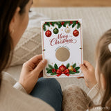 A festive white merry christmas scratch reveal card decorated with red green and gold baubles holly and a bow