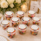 Clear plastic tubs filled with colorful gummy candies sealed with white monogram wreath foiled stickers and gold lettering